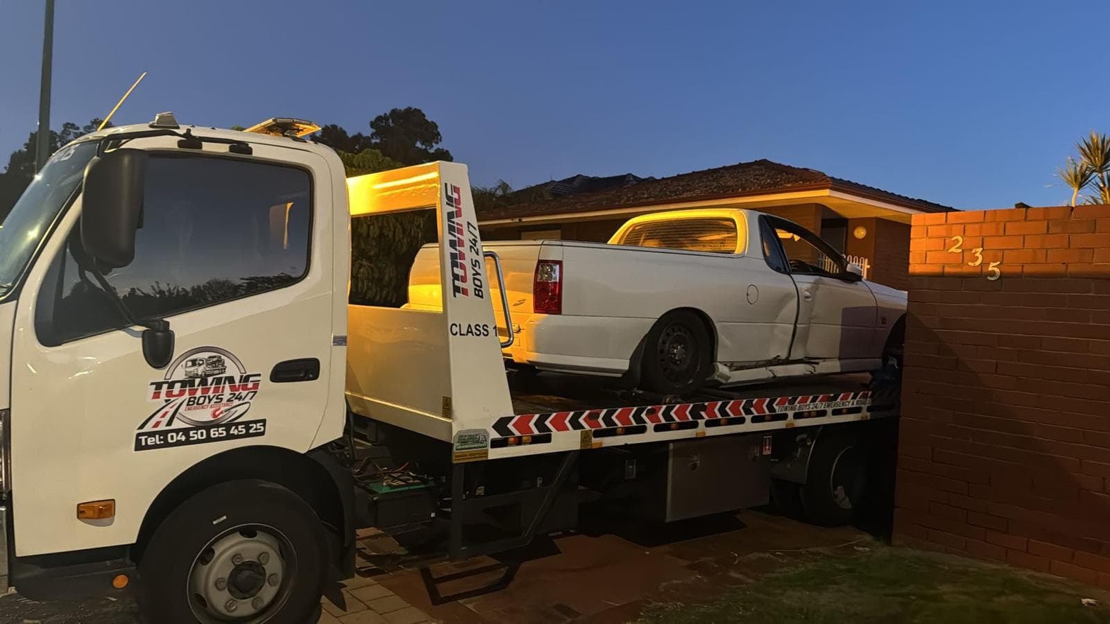 Tow truck recovering a crash-damaged ute at dusk in a Perth driveway